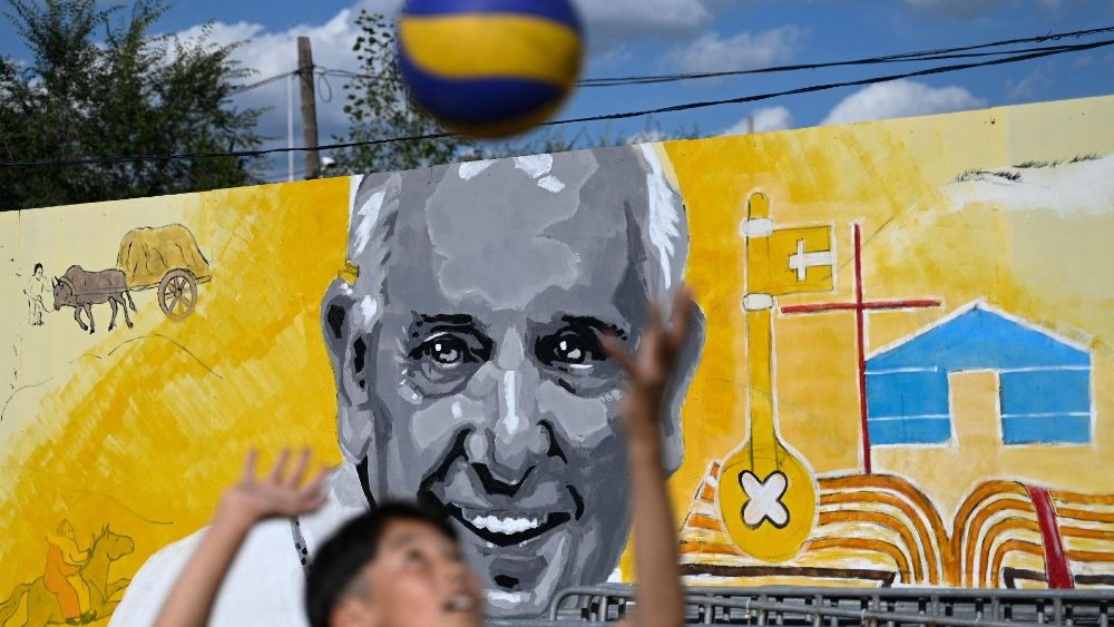 Menino mongol com uma bola diante de um painel  alusivo à visita do Papa Francisco, em frente à Catedral São Pedro e São Paulo em Ulan Bator. (Photo by Pedro Pardo/AFP)