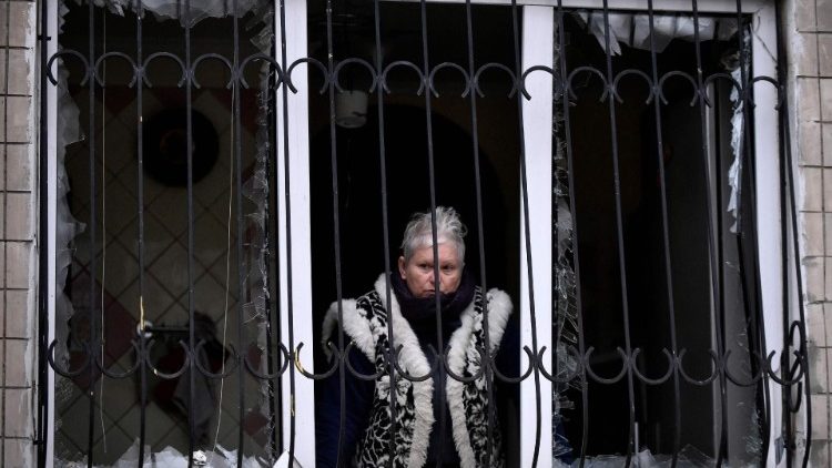 Uma mulher olha através de uma janela quebrada de um prédio residencial danificado após um ataque com mísseis em Kiev, em 13 de dezembro de 2023, em meio à invasão russa da Ucrânia. (Foto de SERGEI CHUZAVKOV/AFP)