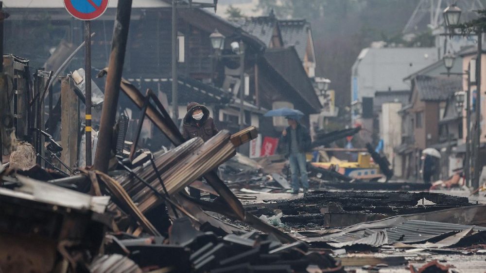 Pessoas caminham perto da área onde ficava o Mercado Matinal de Wajima antes de um incêndio induzido pelo terremoto devastar a área, na cidade de Wajima, província de Ishikawa, em 3 de janeiro de 2024, (Foto de JIJI Press / AFP) 
