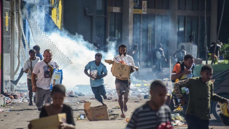Pessoas correm com mercadorias enquanto multidões saem das lojas com produtos saqueados em Port Moresby, em 10 de janeiro de 2024. (Foto da AFP)
