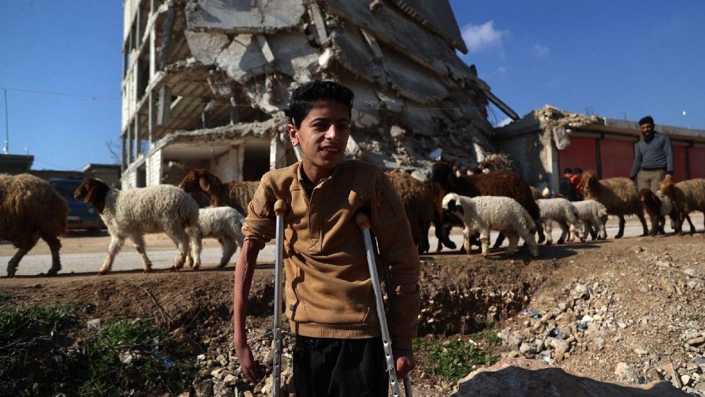 O sobrevivente do terremoto sírio, Hamza Al-Ahmed, passa por prédios destruídos no campo onde mora, na cidade de Jindayris, no noroeste da província de Aleppo, em 4 de fevereiro de 2024. (Foto de Aaref WATAD/AFP)