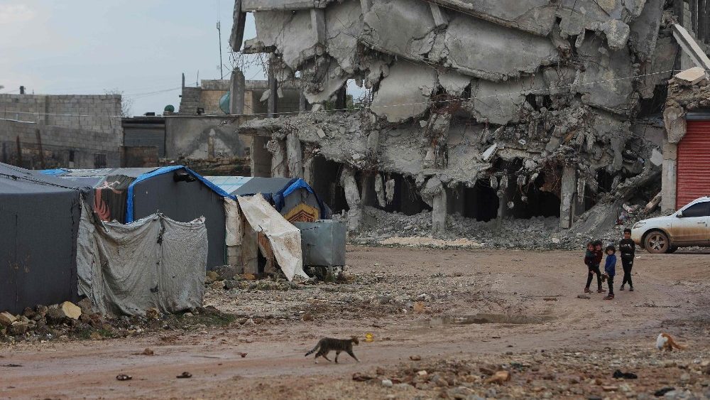 Crianças passam por um prédio destruído próximo a tendas montadas em um campo para sírios deslocados pelo terremoto na cidade de Jindayris, no noroeste da província de Aleppo, em 3 de fevereiro de 2024.. (Foto de Aaref WATAD/AFP)
