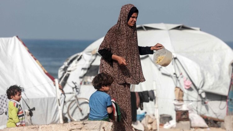 Una donna palestinese cammina vicino alle tende di un campo  per sfollati nel sud della Striscia di Gaza (AFP)