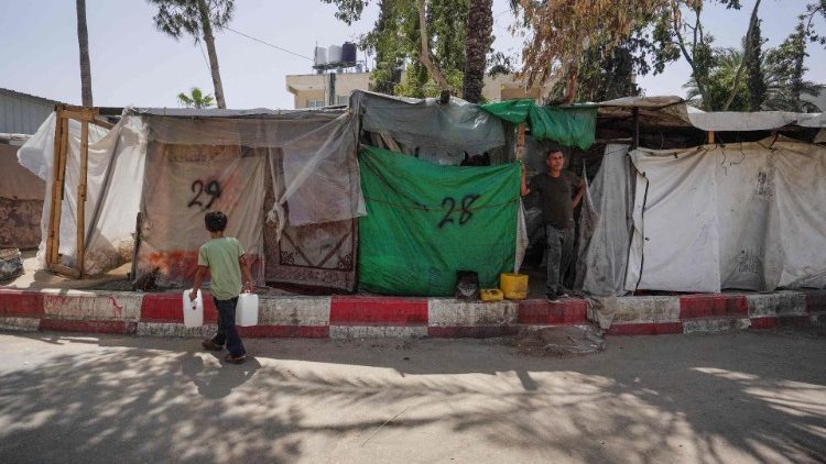 A displaced Palestinian boy carries jerricans of water as he walks in front of tents set up inside the European hospital compound in Khan Yunis