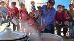 Crianças aguardam a distribuição de alimentos em um acampamento, onde vivem devido ao bombardeio israelense na Faixa de Gaza (AFP)