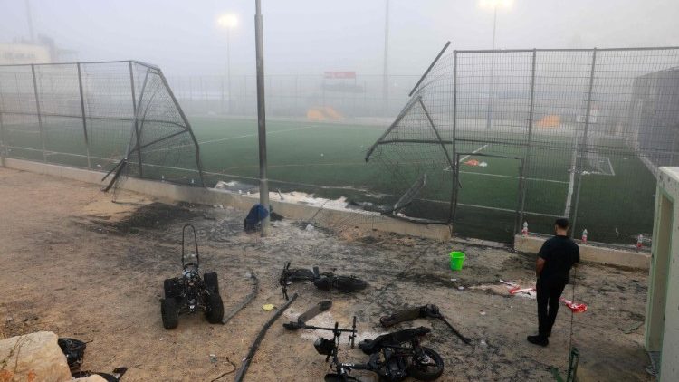 Uma cerca danificada e destroços são vistos em um campo de futebol após um foguete vindo do Líbano ter caído na vila de Majdal Shams na área de Golã anexada por Israel em 28 de julho de 2024. (Foto de Menahem Kahana / AFP)