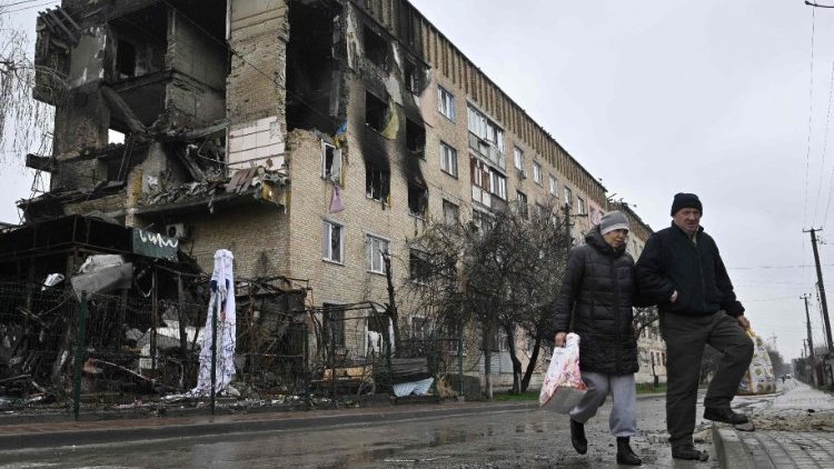 Pedestres passam por um prédio residencial danificado na vila de Gostomel, perto de Kiev, em 22 de abril de 2022, em meio à invasão militar da Rússia lançada na Ucrânia. (Foto de Genya SAVILOV / AFP)