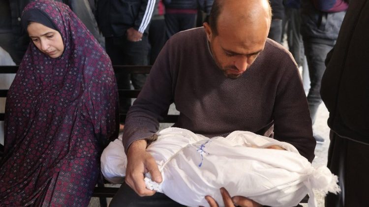 A Palestinian man mourns as he carries the shrouded body of a child ahead of a funeral