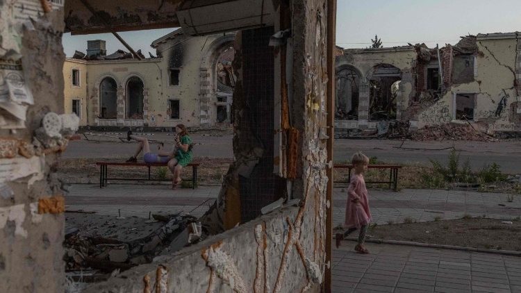Uma criança brinca enquanto mulheres descansam em um banco em frente a prédios residenciais destruídos por bombardeios em Kostyantynivka, região oriental de Donetsk, em 22 de junho de 2024, em meio à invasão russa da Ucrânia. (Foto de Roman PILIPEY / AFP) - UKRAINE-RUSSIA-CONFLICT-WAR-3 YEARS