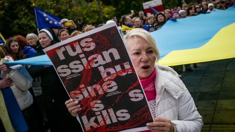 Uma ucraniana que vive na Grécia segura um cartaz coberto de sangue falso enquanto se manifesta em apoio à Ucrânia na véspera do terceiro aniversário da invasão russa ao país, no centro de Atenas, em 23 de fevereiro de 2025. (Foto de Aris MESSINIS / AFP)