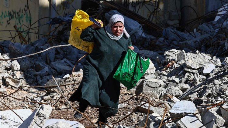 Uma mulher carrega sacolas enquanto caminha sobre escombros no campo de refugiados palestinos de Nur Shams, perto de Tulkarem, onde as forças israelenses permitiram que os moradores recuperassem seus pertences após emitirem notificações de demolição de várias casas, em meio a uma ofensiva de semanas na Cisjordânia ocupada em 26 de fevereiro de 2025. (Foto de Zain JAAFAR / AFP)