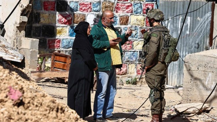 Palestinos conversam com um soldado israelense no campo de refugiados palestinos de Nur Shams, perto de Tulkarem, onde o exército permitiu que os moradores recuperassem seus pertences após emitir notificações de demolição de várias casas, em meio a uma ofensiva de semanas na Cisjordânia ocupada em 26 de fevereiro de 2025. (Foto de Zain JAAFAR / AFP)