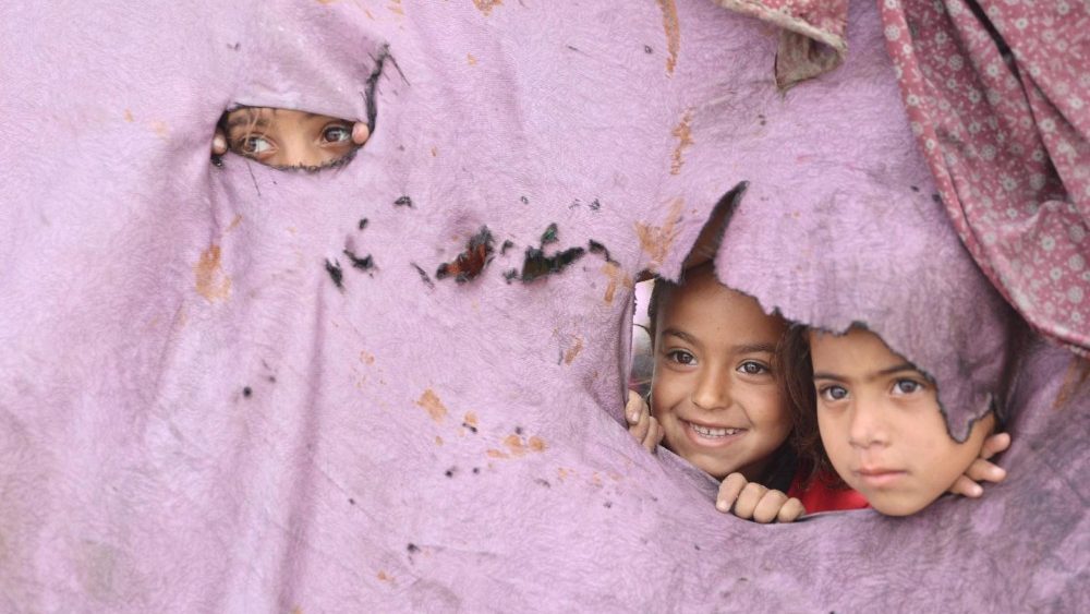 Crianças palestinas espiam pelos buracos de sua barraca em um campo de deslocados improvisado, montado em meio aos escombros de um prédio na Cidade de Gaza, em 12 de maio de 2025. O primeiro-ministro israelense, Benjamin Netanyahu, disse em 12 de maio que a libertação de um refém israelense-americano anunciada pelo Hamas não levaria a um cessar-fogo na Faixa de Gaza nem à libertação de detidos palestinos. (Foto de Omar AL-QATTAA / AFP)