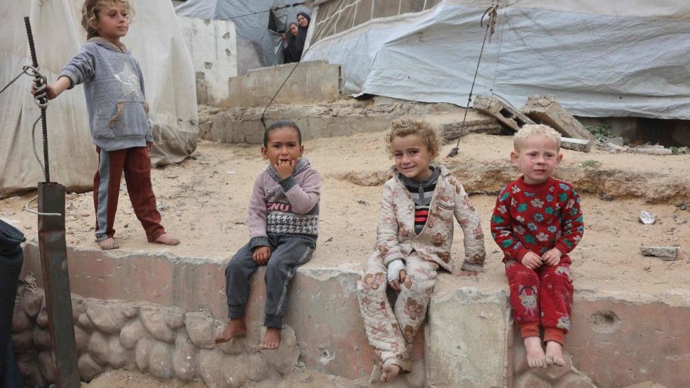 Crianças palestinas sentam-se perto de tendas em um campo de deslocados improvisado, montado em meio aos escombros de um prédio na Cidade de Gaza, em 12 de maio de 2025. O primeiro-ministro israelense, Benjamin Netanyahu, disse em 12 de maio que a libertação de um refém israelense-americano anunciada pelo Hamas não levaria a um cessar-fogo na Faixa de Gaza nem à libertação de detidos palestinos. (Foto de Omar AL-QATTAA / AFP)