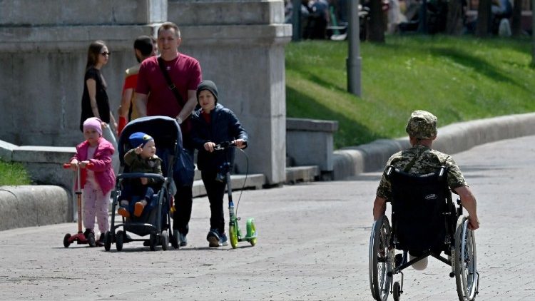 A wounded Ukrainian serviceman on a wheelchair rides past a family in the capital of Kyiv on June 15, 2025, amid Russian invasion in Ukraine. (Photo by Sergei SUPINSKY / AFP)