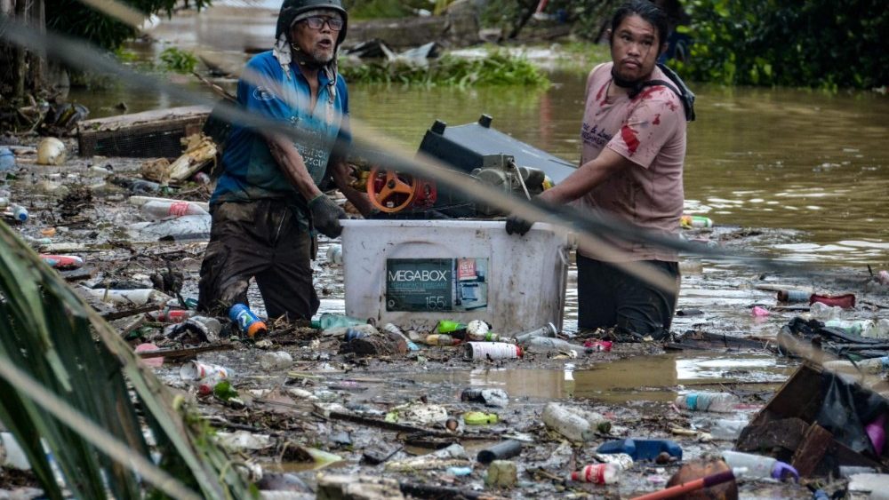 Moradores carregando seus pertences atravessam uma rua alagada enquanto evacuam suas casas inundadas na cidade de Liloan, província de Cebu, em 4 de novembro de 2025, após a passagem do tufão Kalmaegi durante a noite. Moradores buscaram refúgio em telhados e carros flutuaram pelas ruas alagadas em 4 de novembro, enquanto o tufão Kalmaegi castigava a região central das Filipinas, deixando pelo menos duas pessoas mortas. (Foto de Alan TANGCAWAN / AFP)