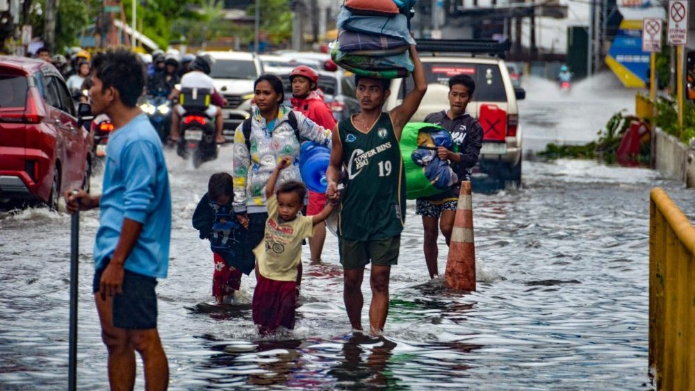 Moradores carregando seus pertences atravessam uma rua alagada na cidade de Mandaue, província de Cebu, em 4 de novembro de 2025, após a passagem do tufão Kalmaegi durante a noite. Moradores buscaram refúgio em telhados e carros flutuaram pelas ruas alagadas em 4 de novembro, enquanto o tufão Kalmaegi castigava a região central das Filipinas, deixando pelo menos duas pessoas mortas. (Foto de Alan TANGCAWAN / AFP)