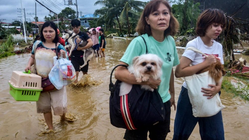Moradores carregando seus pertences e cães de estimação atravessam uma rua alagada enquanto evacuam suas casas inundadas na cidade de Liloan, província de Cebu, em 4 de novembro de 2025, após a passagem do tufão Kalmaegi durante a noite. Moradores buscaram refúgio em telhados e carros flutuaram pelas ruas alagadas em 4 de novembro, enquanto o tufão Kalmaegi castigava a região central das Filipinas, deixando pelo menos duas pessoas mortas. (Foto de Alan TANGCAWAN / AFP)