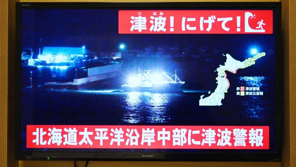 Um alerta de tsunami é emitido enquanto imagens ao vivo de um barco deixando um porto costeiro são exibidas em uma televisão em Sapporo, na província de Hokkaido, no norte do Japão, em 8 de dezembro de 2025. O Japão registrou um tsunami de 40 centímetros (16 polegadas) após um terremoto de magnitude 7,6 em 8 de dezembro. (Foto de GREG BAKER / AFP)