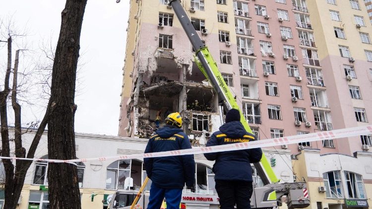 Equipes de resgate ucranianas est&atilde;o em frente a um pr&eacute;dio residencial danificado ap&oacute;s um ataque de drones e m&iacute;sseis russos em Kiev, em 27 de dezembro de 2025, em meio &agrave; invas&atilde;o russa na Ucr&acirc;nia. Diversas explos&otilde;es poderosas sacudiram Kiev em 27 de dezembro de 2025, enquanto as autoridades alertavam que a capital ucraniana estava sob amea&ccedil;a de ataque com m&iacute;sseis. (Foto de Serhii Okunev / AFP)