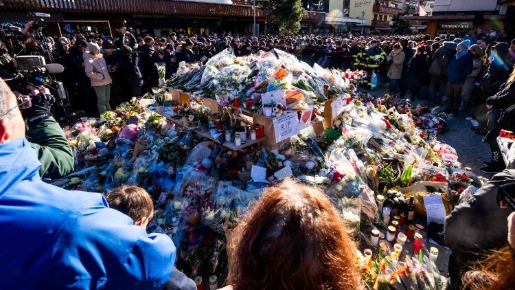 Pessoas se reúnem em torno de um memorial improvisado para prestar suas homenagens, depositando flores, velas e mensagens perto do bar Constellation, em Crans-Montana, no dia 4 de janeiro de 2026, em memória das vítimas do incêndio que devastou o estabelecimento na luxuosa estação de esqui alpina na véspera de Ano Novo. (Foto de MAXIME SCHMID / AFP)