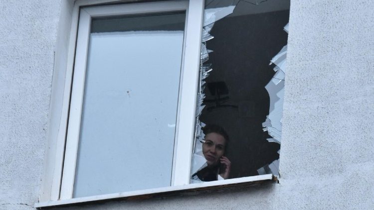 Uma mulher, falando ao celular, olha pela janela quebrada de um apartamento em um pr&eacute;dio residencial danificado ap&oacute;s um ataque de drone em Dnipro, em 7 de janeiro de 2026, durante a invas&atilde;o russa na Ucr&acirc;nia. (Foto de Mykola Synelnykov / AFP)