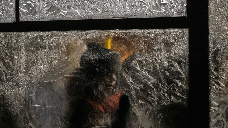Um menino tenta remover o gelo de uma janela congelada enquanto anda de &ocirc;nibus em uma noite de inverno em Kiev, em 15 de janeiro de 2026, em meio &agrave; invas&atilde;o russa da Ucr&acirc;nia. (Foto de Sergei Gapon / AFP)