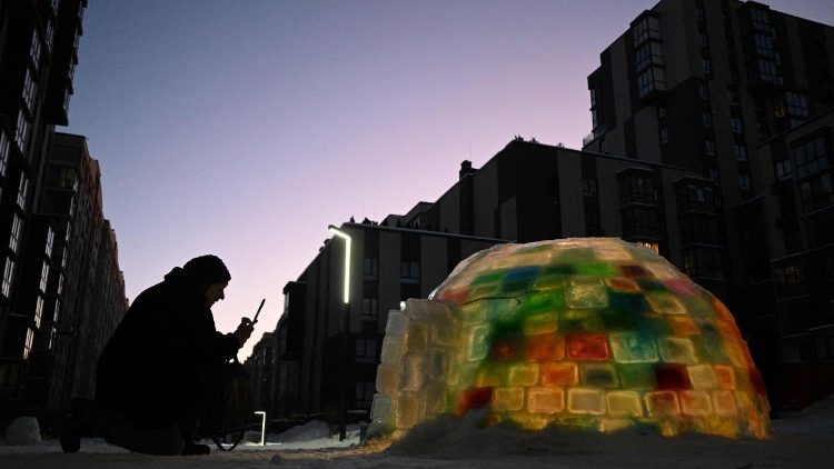 Uma mulher fotografa um iglu de gelo constru&iacute;do por moradores locais no p&aacute;tio de um pr&eacute;dio residencial em Lviv, em 18 de janeiro de 2026, em meio &agrave; invas&atilde;o russa da Ucr&acirc;nia. (Foto de YURIY DYACHYSHYN / AFP)