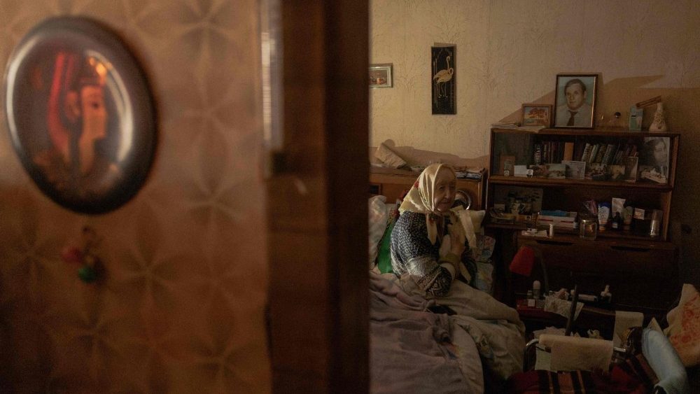 Esfir Rudminska, aposentadade 88 anos, senta-se em uma cama em seu apartamento sem eletricidade e quase sem aquecimento, em Kiev, em 26 de janeiro de 2026, após ataques com mísseis e drones à infraestrutura energética ucraniana em meio à invasão russa na Ucrânia. A Rússia intensificou neste mês seus ataques contra a infraestrutura de energia e aquecimento da Ucrânia, mergulhando os moradores de Kiev na escuridão e no frio, com temperaturas chegando a -20°C. (Foto de Roman PILIPEY / AFP)