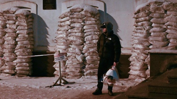 Um homem segurando flores est&aacute; ao lado de um pr&eacute;dio com as janelas protegidas por sacos de areia contra poss&iacute;veis danos causados ​​por ataques a&eacute;reos em Kiev, em 29 de janeiro de 2026, em meio &agrave; invas&atilde;o russa da Ucr&acirc;nia. (Foto de Sergei Gapon / AFP)