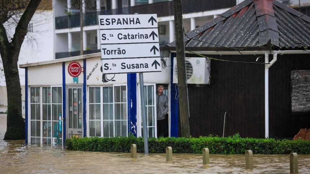 A man stands at the door of his establishment surrounded by water in Alcacer do Sal, south of Portugal, where floods are expected during Leonardo storm on February 4, 2026. The Iberian peninsula on February 4, 2026 braced for a violent storm, with southern Spain shutting schools and Portugal placed on fresh alert after severe weather killed five people last week. (Photo by PATRICIA DE MELO MOREIRA / AFP)