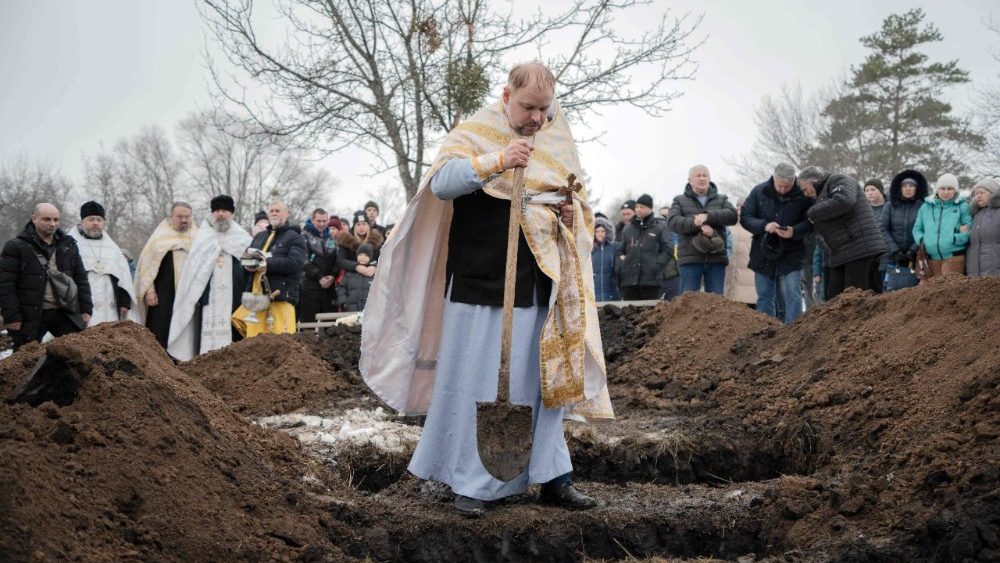 Um sacerdote ucraniano joga punhados de terra sobre os caixões durante o funeral de Grigory Shikula, de 34 anos, seus dois filhos, Ivan e Vladislav, e sua filha, Myroslava, que foram mortos por um ataque de drone russo em um cemitério na vila de Skovorodynivka, na região de Kharkiv, em 13 de fevereiro de 2026, em meio à invasão russa da Ucrânia. Um ataque de drone russo a uma casa no nordeste da Ucrânia, em 11 de fevereiro de 2026, matou três crianças pequenas e seu pai, além de ferir a mãe grávida, disseram autoridades. Gêmeos de um ano e uma menina de dois anos foram mortos no ataque noturno à casa da família na cidade de Bogodukhiv, a cerca de 20 quilômetros da fronteira com a Rússia. (Foto de Ivan SAMOILOV / AFP)   (AFP or licensors)