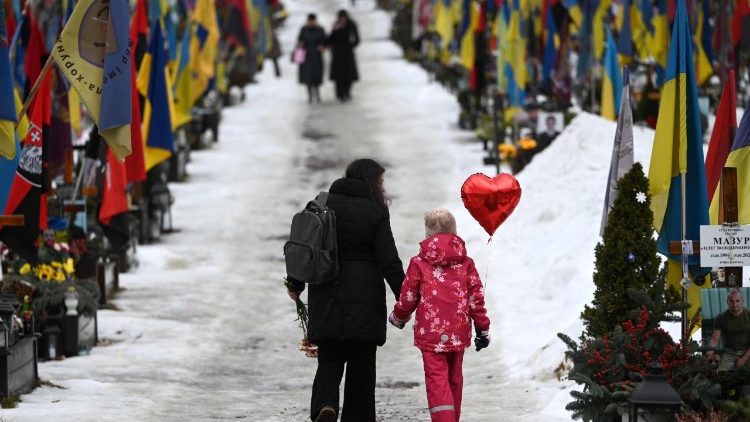 Uma m&atilde;e e sua filha caminham segurando um bal&atilde;o em forma de cora&ccedil;&atilde;o no Cemit&eacute;rio Militar de Lychakiv, em Lviv, no Dia dos Namorados, em 14 de fevereiro de 2026, em meio &agrave; invas&atilde;o russa da Ucr&acirc;nia. (Foto de YURIY DYACHYSHYN / AFP)