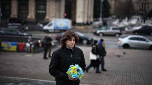 A resìdent of Kyiv carries a bouquet of flowers to lay at a makeshift memorial for Ukrainian and foreign soldiers