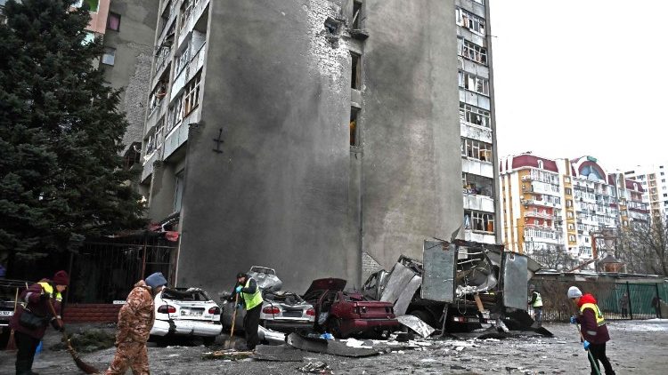 Trabalhadores comunit&aacute;rios removem os destro&ccedil;os ao lado de carros destru&iacute;dos no p&aacute;tio de um pr&eacute;dio residencial danificado ap&oacute;s um ataque a&eacute;reo em Kharkiv, em 26 de fevereiro de 2026, em meio &agrave; invas&atilde;o russa da Ucr&acirc;nia. Ataques russos em v&aacute;rias cidades ucranianas feriram 23 pessoas, incluindo uma crian&ccedil;a, disseram autoridades em 26 de fevereiro de 2026, antes das negocia&ccedil;&otilde;es entre representantes ucranianos e americanos em Genebra, com o objetivo de p&ocirc;r fim &agrave; guerra de Moscou. (Foto de SERGEY BOBOK / AFP)