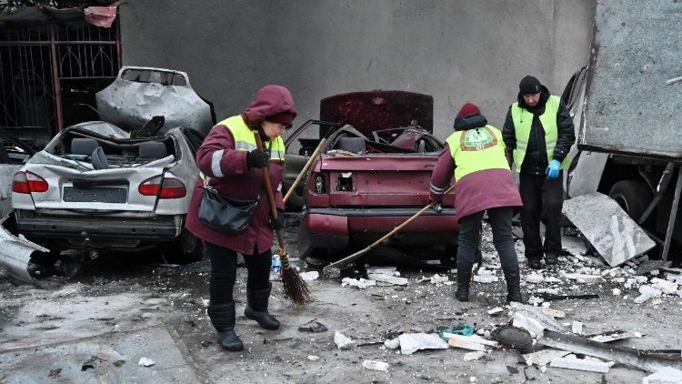 Trabalhadores comunit&aacute;rios removem os destro&ccedil;os ao lado de carros destru&iacute;dos no p&aacute;tio de um pr&eacute;dio residencial danificado ap&oacute;s um ataque a&eacute;reo em Kharkiv, em 26 de fevereiro de 2026, em meio &agrave; invas&atilde;o russa da Ucr&acirc;nia. Ataques russos em v&aacute;rias cidades ucranianas feriram 23 pessoas, incluindo uma crian&ccedil;a, disseram autoridades em 26 de fevereiro de 2026, antes das negocia&ccedil;&otilde;es entre representantes ucranianos e americanos em Genebra, com o objetivo de p&ocirc;r fim &agrave; guerra de Moscou. (Foto de SERGEY BOBOK / AFP)
