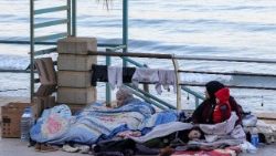 A displaced woman and her children sit near the sea at a makeshift encampment in Beirut