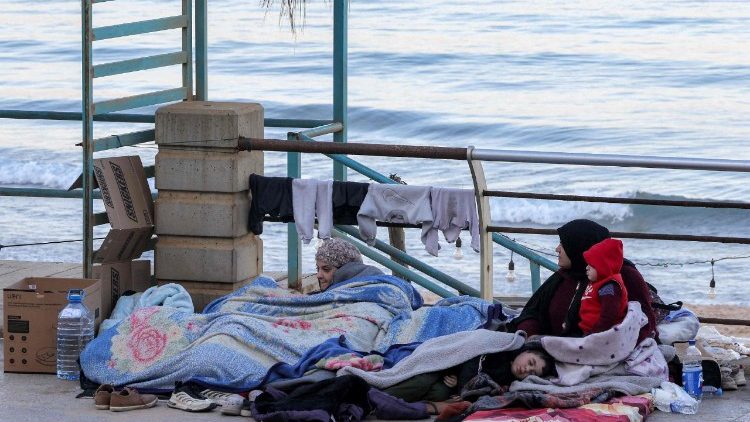 A displaced woman and her children sit near the sea at a makeshift encampment in Beirut