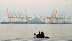 Una famiglia siede sullo sfondo di un cantiere navale al largo della città costiera di Fujairah, nello Stretto di Hormuz