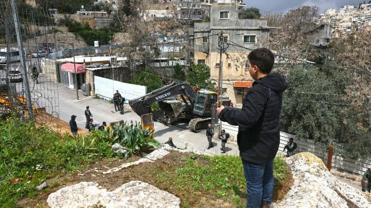 A boy looks at Israeli security forces patrolling as Jerusalem municipality workers prepare to demolish a house belonging to a Palestinian family