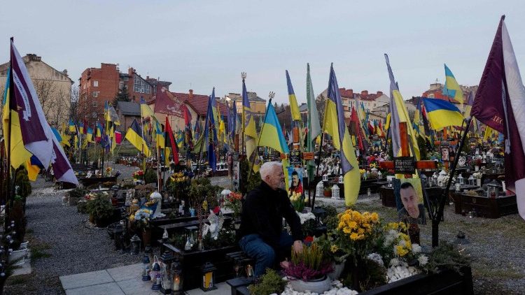 Oleksiy Kravchuk, 62, diretor art&iacute;stico do Teatro Acad&ecirc;mico de Lviv "People and Dolls", diretor, ator e veterano, senta-se no t&uacute;mulo de seu companheiro de armas ca&iacute;do no Cemit&eacute;rio Militar de Lychakiv, em Lviv, em 25 de mar&ccedil;o de 2026, em meio &agrave; invas&atilde;o russa da Ucr&acirc;nia. Quando Oleksiy Kravchuk ingressou no ex&eacute;rcito ucraniano no in&iacute;cio da invas&atilde;o russa em 2022, lutou como atirador de elite e era conhecido por seu apelido militar, S&atilde;o Nicolau. Ferido em combate em maio de 2022 no leste da Ucr&acirc;nia, ele come&ccedil;ou a evacuar os corpos de seus colegas que tiveram menos sorte – aqueles mortos no campo de batalha – antes de ser dispensado aos 60 anos. Desde ent&atilde;o, ele vem recontando sua vida como civil e soldado por meio de hist&oacute;rias teatrais narradas com figuras brancas e delicadas feitas de papel. (Foto de Tetiana DZHAFAROVA / AFP)