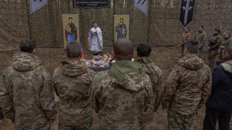 O capel&atilde;o militar Mykola Bahirov reza com membros do 33&ordm; Batalh&atilde;o Mecanizado Independente da Ucr&acirc;nia, ao lado de bolos e outros alimentos tradicionais, para celebrar a P&aacute;scoa Ortodoxa, na regi&atilde;o de Kharkiv, em 12 de abril de 2026, em meio &agrave; invas&atilde;o russa da Ucr&acirc;nia. Greco-cat&oacute;lico, este homem de 39 anos trabalhava como secret&aacute;rio diocesano quando a R&uacute;ssia lan&ccedil;ou sua invas&atilde;o em grande escala da Ucr&acirc;nia, em fevereiro de 2022. Foi no funeral de um soldado, ao presenciar o terror nas filhas do falecido, que Mykola Bahirov decidiu se tornar capel&atilde;o: em vez de acompanh&aacute;-las na morte, ele permaneceria, enquanto elas ainda estivessem vivas, perto dos soldados ucranianos que lutavam contra o invasor russo. (Foto de Roman PILIPEY / AFP)