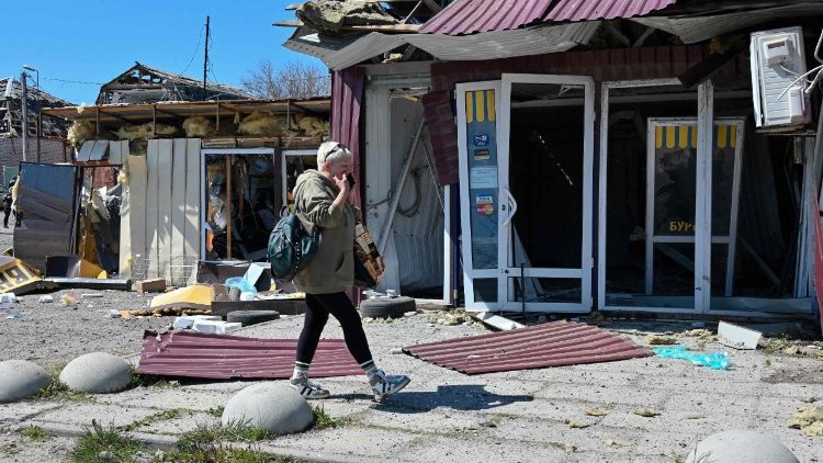 Uma mulher caminha ao lado de lojas danificadas no local de um ataque de m&iacute;ssil russo na cidade de Merefa, regi&atilde;o de Kharkiv, em 4 de maio de 2026, em meio &agrave; invas&atilde;o russa da Ucr&acirc;nia. O ataque atingiu a cidade de Merefa, que sofreu intensos ataques da R&uacute;ssia nos mais de quatro anos de invas&atilde;o. (Foto de SERGEY BOBOK / AFP)
