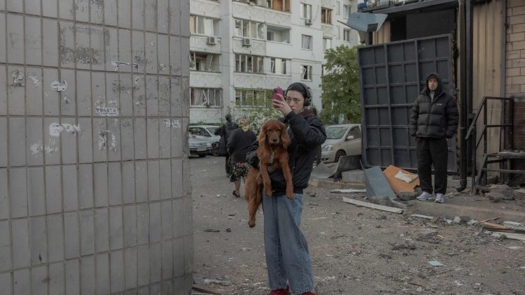 Uma mulher segurando seu cachorro fotografa um pr&eacute;dio residencial parcialmente destru&iacute;do ap&oacute;s ataques de drones e m&iacute;sseis russos em Kiev, em 14 de maio de 2026, em meio &agrave; invas&atilde;o russa na Ucr&acirc;nia. A capital ucraniana sofreu um intenso ataque a&eacute;reo no in&iacute;cio da manh&atilde; de 14 de maio, conforme relatado por um jornalista da AFP, enquanto o prefeito de Kiev afirmava que a R&uacute;ssia estava atacando a cidade. (Foto de Roman PILIPEY / AFP)