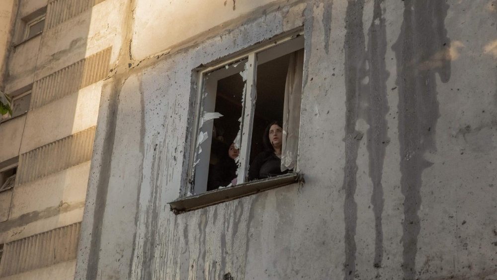 Moradores observam a paisagem através de uma janela quebrada em um prédio residencial de vários andares, danificado após ataques com mísseis e drones russos contra Kiev em 2 de junho de 2026, durante a invasão russa da Ucrânia. A Rússia disparou mais de 600 drones e dezenas de mísseis — incluindo mísseis balísticos de difícil abate — contra a Ucrânia, informou a Força Aérea de Kiev em 2 de junho de 2026, em um bombardeio noturno que matou pelo menos nove pessoas. (Foto de Roman PILIPEY / AFP)