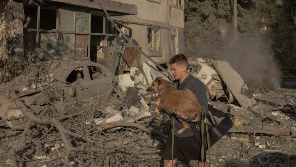 Um homem carrega um cachorro nos braços em meio aos escombros de um prédio residencial de vários andares danificado por ataques de mísseis e drones russos contra Kiev em 2 de junho de 2026, durante a invasão russa da Ucrânia. A Rússia disparou mais de 600 drones e dezenas de mísseis — incluindo mísseis balísticos de difícil abate — contra a Ucrânia, informou a Força Aérea de Kiev em 2 de junho de 2026, em um bombardeio noturno que matou pelo menos nove pessoas. (Foto de Roman PILIPEY / AFP)