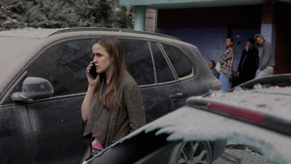 Uma mulher fala ao telefone ao lado de carros danificados após um ataque de mísseis russos à capital ucraniana, Kiev, em 6 de julho de 2026, em meio à invasão russa na Ucrânia. A Rússia atacou a região de Kiev, na Ucrânia, com mísseis balísticos em 6 de julho. (Foto de Tetiana DZHAFAROVA / AFP)