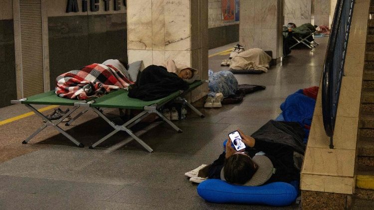 Uma pessoa verifica um smartphone enquanto outras dormem, abrigando-se durante a noite em uma esta&ccedil;&atilde;o de metr&ocirc; de Kiev, ap&oacute;s alertas de um poss&iacute;vel ataque a&eacute;reo russo, no in&iacute;cio da manh&atilde; de 10 de agosto de 2026, em meio &agrave; invas&atilde;o russa da Ucr&acirc;nia. (Foto de Serhii Okunev / AFP)