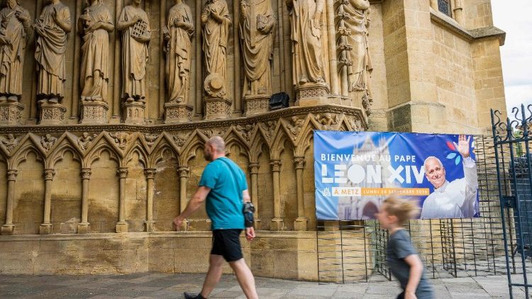 Visitantes passam por um cartaz  com os dizeres "Bem-vindo ao Papa Leão XIV" dentro da Catedral de Saint-Étienne em Metz, no leste da França, em 19 de agosto de 2026. (Foto de Jean-Christophe Verhaegen / AFP)