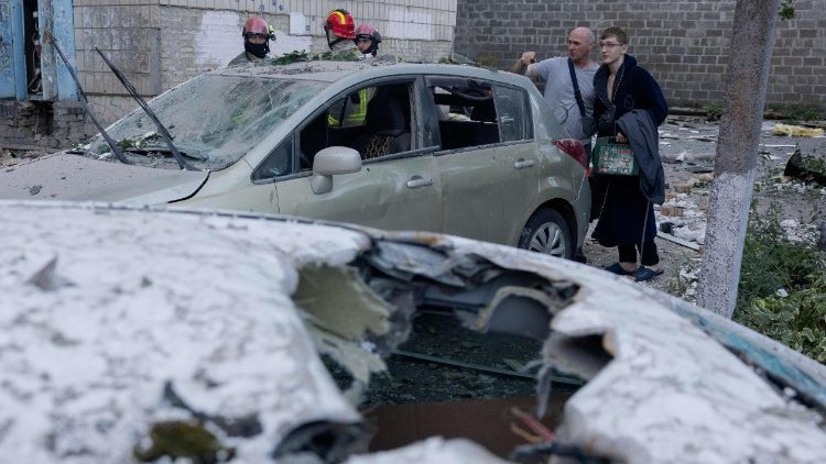 Pessoas observam carros danificados ap&oacute;s um ataque russo em Kiev, em 20 de agosto de 2026, durante a invas&atilde;o da Ucr&acirc;nia pela R&uacute;ssia. O bombardeio russo matou seis pessoas e feriu dezenas na capital ucraniana e na regi&atilde;o circundante durante a noite, disseram as autoridades em 20 de agosto. (Foto de Tetiana DZHAFAROVA / AFP)